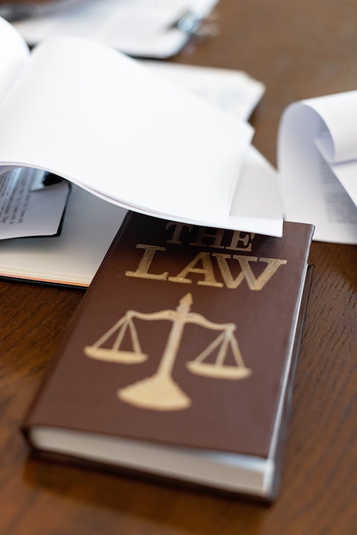 services-04 Close-up of a law book with scales icon on a wooden desk covered in papers.